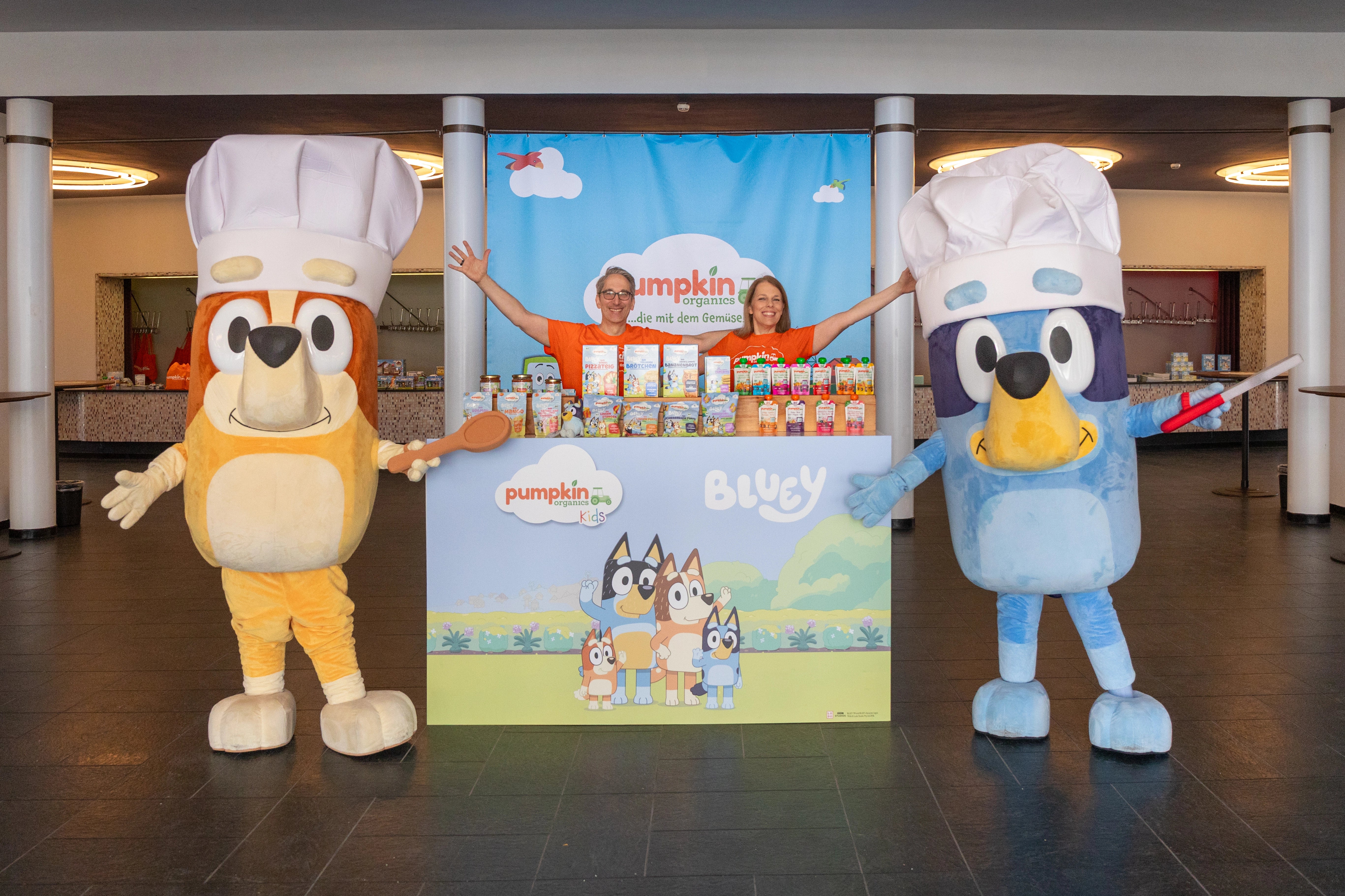 Florian und Jaclyn Schnau sowie die Maskottchen Bluey und Bingo  vor einem Produkt Display von Pumpkin Organics
