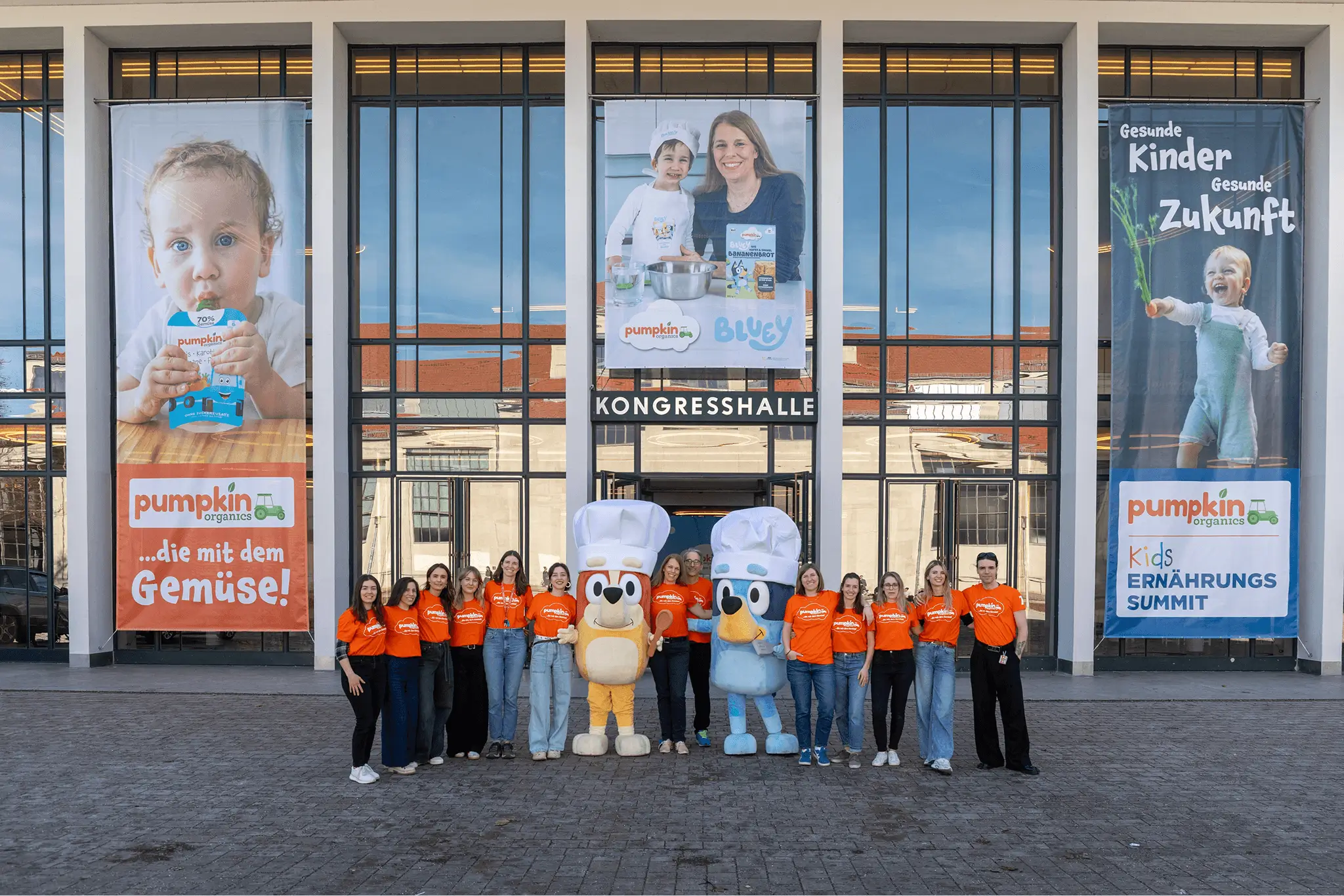 Das Pumpkin Organics Team mit den Maskottchen Bluey und Bingo vor der Alten Kongresshalle in München