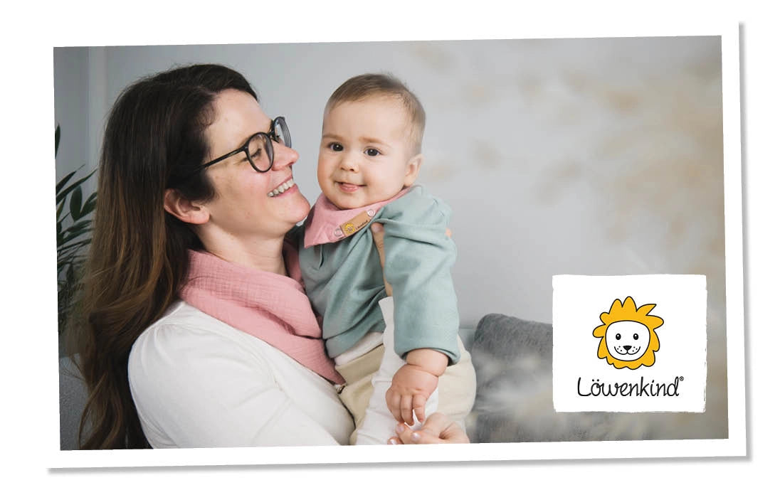Mutter hält ein Baby im Arm, welches ein Halstuch von Löwenkind trägt