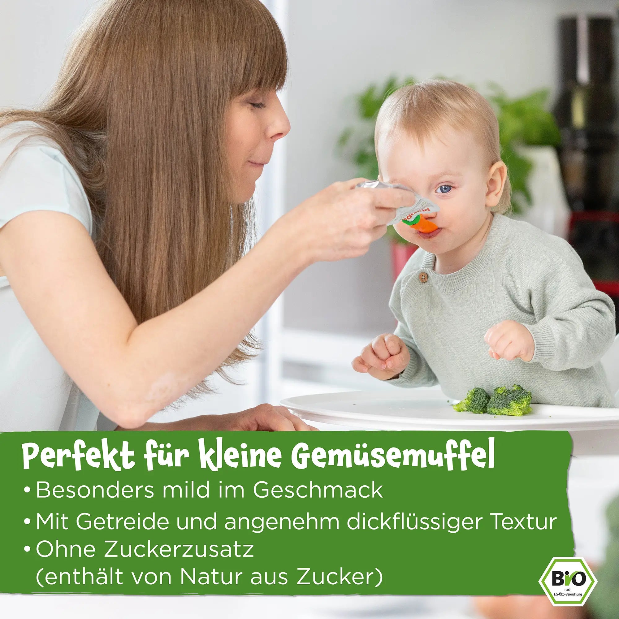 Eine Mutter füttert ihr Baby mit einem Bio Gemüse-Quetschie; Perfekt für kleine Gemüsemuffel; besonders mild im Geschmack; mit Getreide und angenehm dickflüssiger Textur; Ohne Zuckerzusatz (enthält von Natur aus Zucker) 
